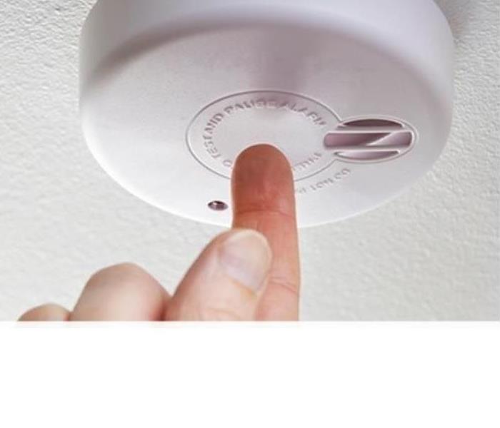 Finger pushing on smoke detector button to test if it works.